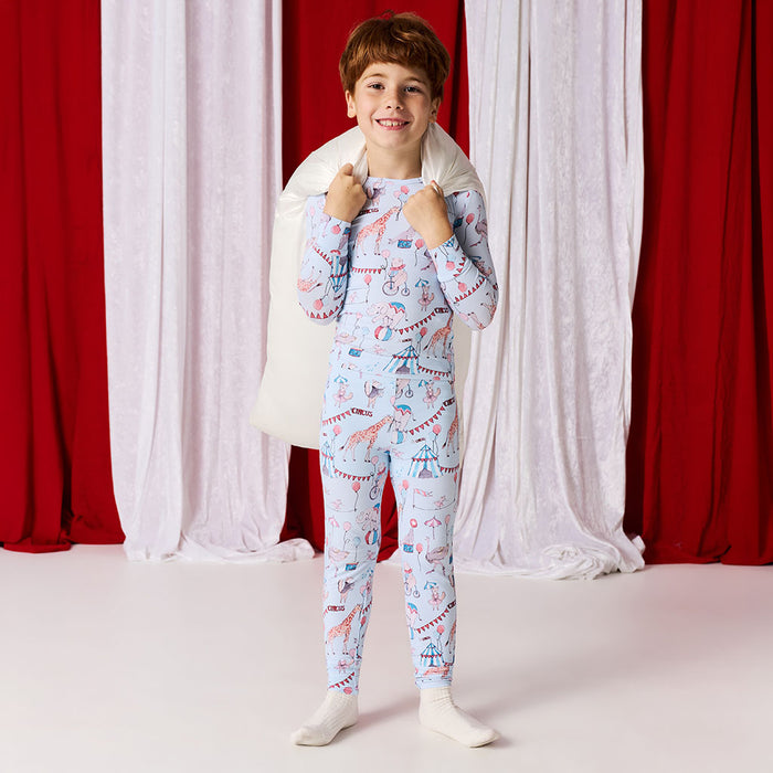 Child wearing a patterned pajama set with a white pillow shoulders against red and white curtains.