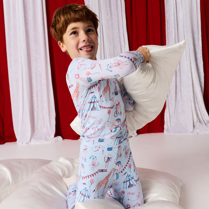 Child in a pajama set with circus design holding a pillow against a red and white curtain background