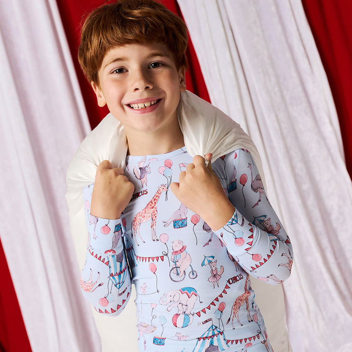 Child wearing pajamas with a circus-themed design in front of red and white curtains.