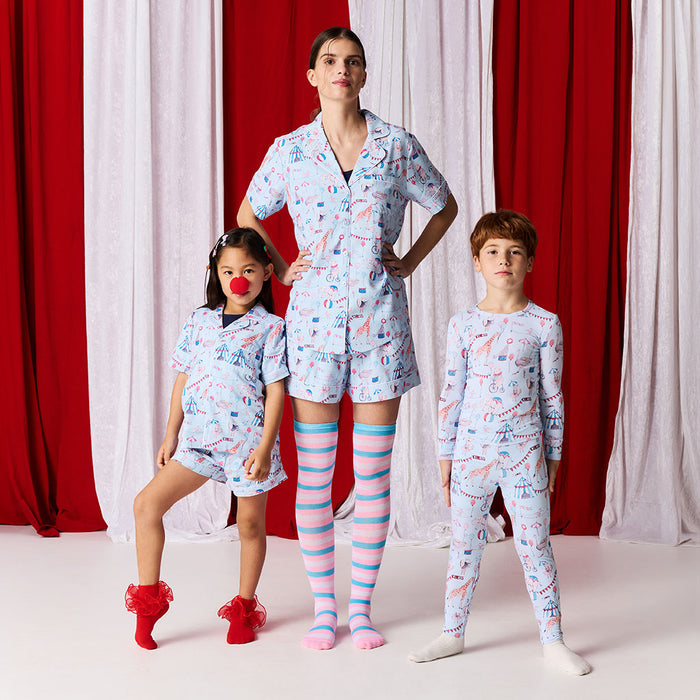 Family of four wearing matching pajama sets in front of red and white curtains.