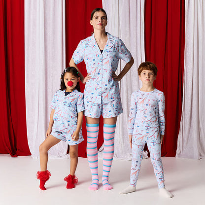 Family of four wearing matching pajama sets in front of red and white curtains.