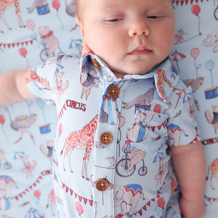 close up of baby wearing circus printed henley shortall with collar and button details with a side chest pocket.