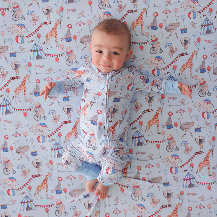 Child wearing a one piece outfit laying against a circus-themed blanket.