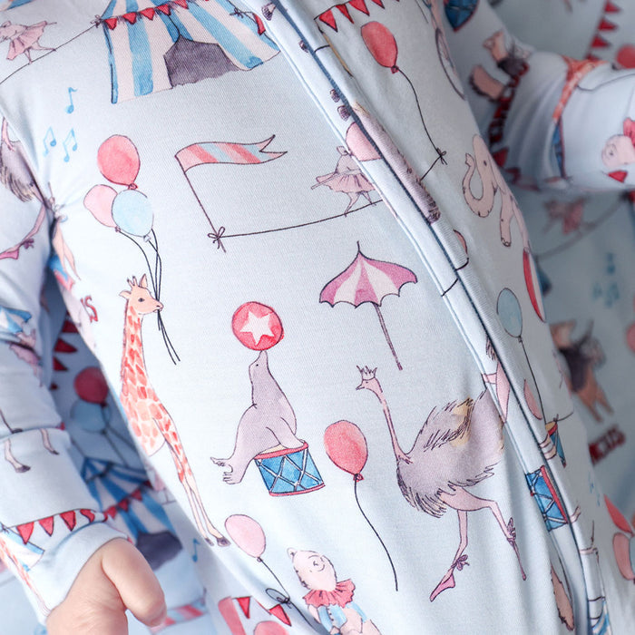 Close up of baby one piece with circus-themed pattern featuring animals and balloons.