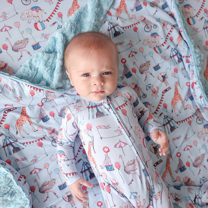 Baby wearing a circus printed one piece lying on a colorful matching blanket with animal patterns