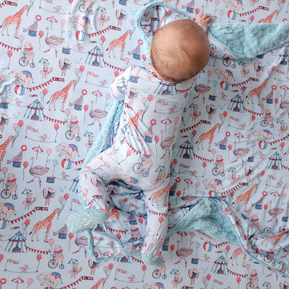 Baby laying wearing a one piece with circus design on a matching blanket