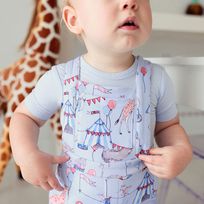 close up of baby wearing circus printed french terry short overalls