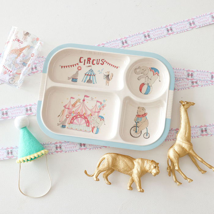 Children's divided plate with circus design on a white surface with decorative items.
