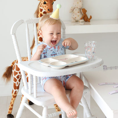 Child in a high chair with a birthday hat, surrounded by toys and a glass cup.