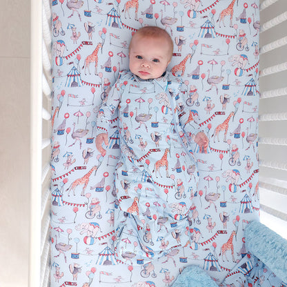 baby wearing a sleeveless sleep bag laying on a matching circus printed crib sheet.