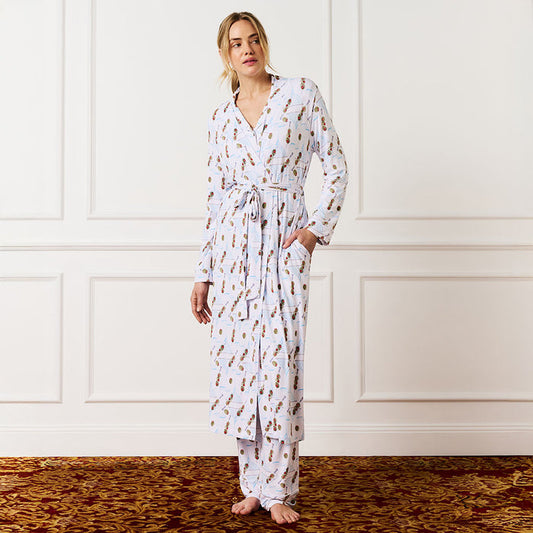 Woman wearing a long, patterned robe standing against a white paneled wall.