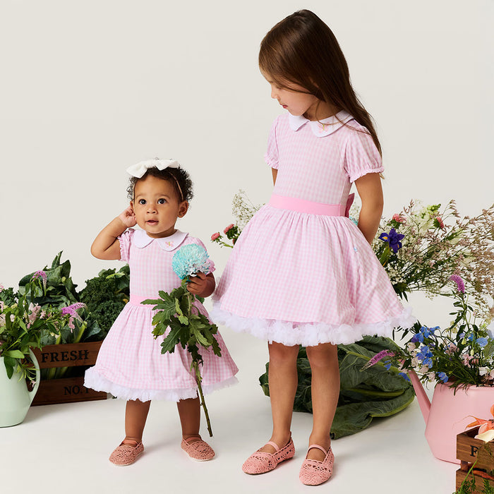 Two young girls in matching pink dresses standing among flowers and plants.