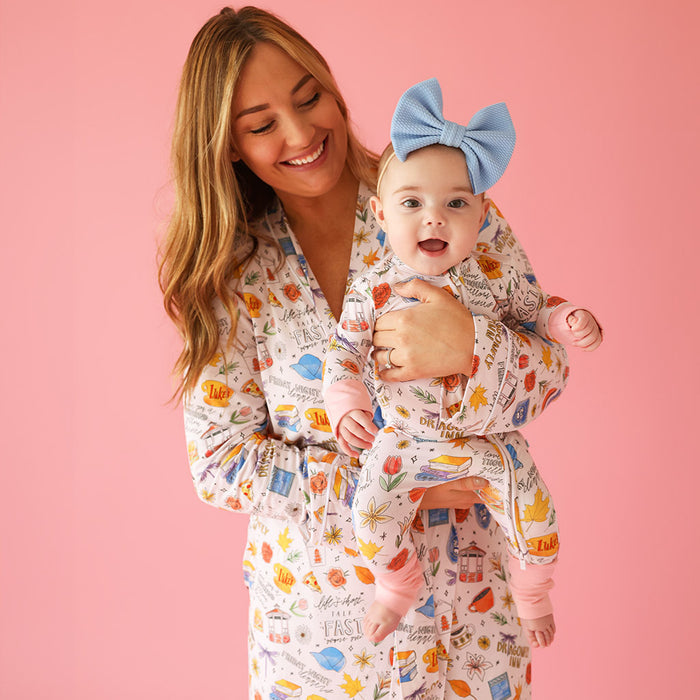 mother holding infant wearing matching Gilmore Girls™ themed print pajamas with pink background