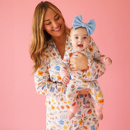 mother holding infant wearing matching Gilmore Girls™ themed print pajamas with pink background