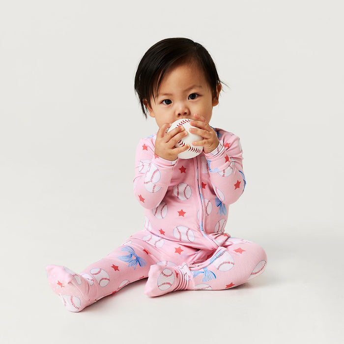 Baby in pink one piece with animal patterns sitting on a light gray background
