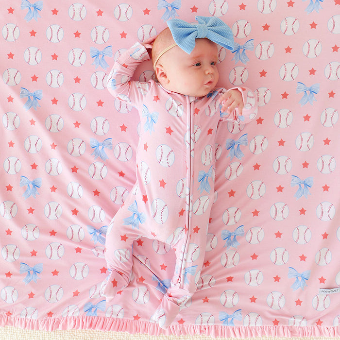 Baby in a pink one piece with blue bows on a pink background with baseball and star patterns