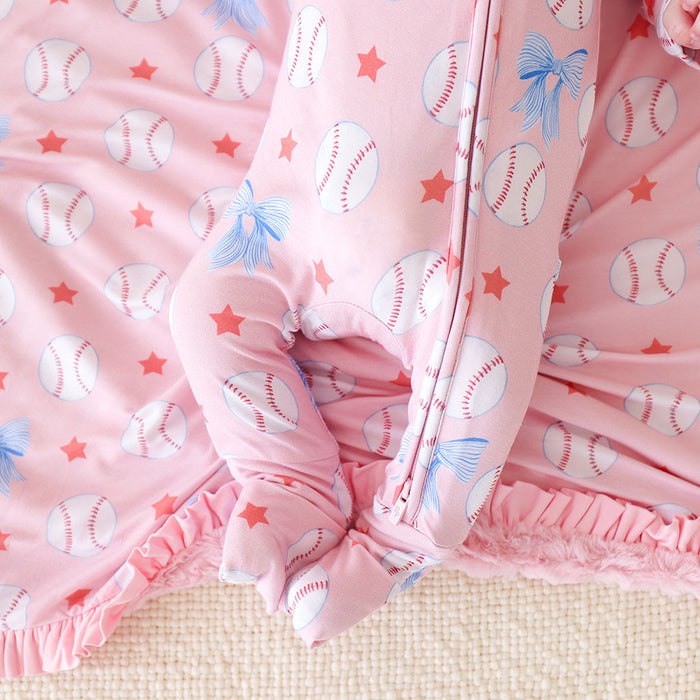 Pink baby blanket with baseball and bow patterns on a textured surface