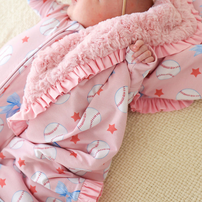 Close-up of a baby in pink one piece with baseball and star patterns on a beige surface.