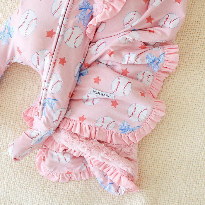 Pink baby one piece with baseball and bow pattern on a beige surface