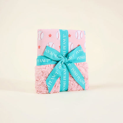 Pink baby blanket with baseball patterns and a blue ribbon on a light beige background