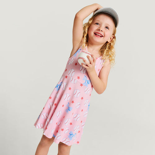 Young girl wearing a pink dress with baseball pattern against a plain background