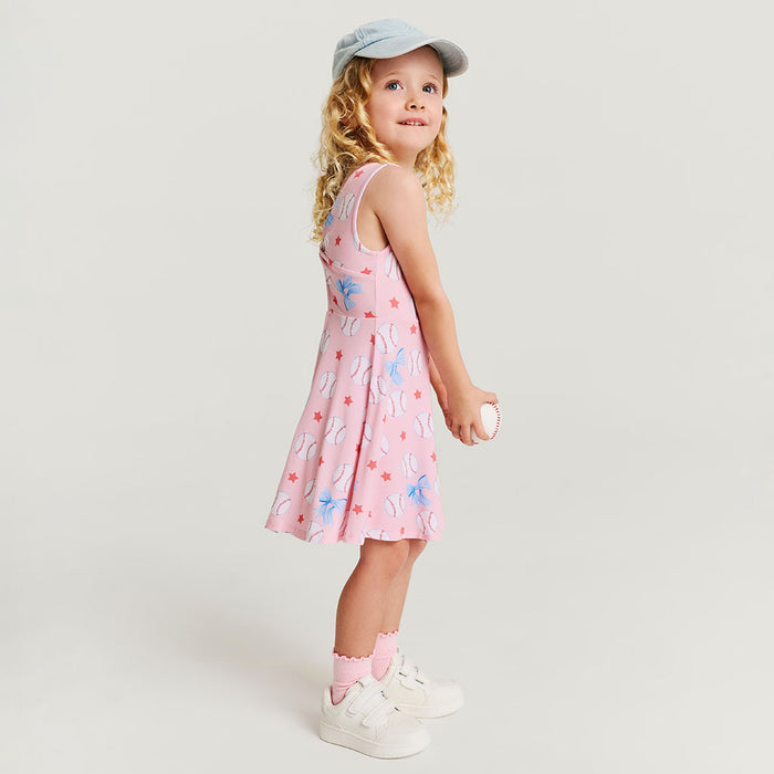 Young girl wearing a pink dress with baseball pattern and white sneakers on a light gray background