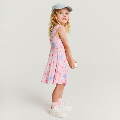 Young girl wearing a pink dress with baseball pattern and white sneakers on a light gray background