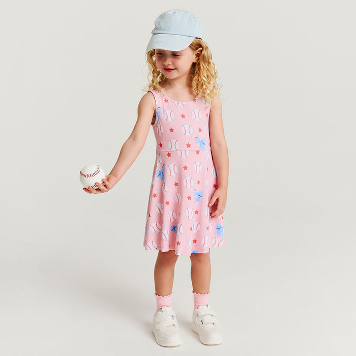 Young girl in a pink dress with baseball pattern holding a baseball, wearing a light blue cap on a white background