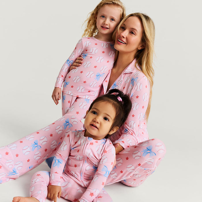 Woman and two children wearing matching pink pajamas with star and baseball patterns on a light gray background.