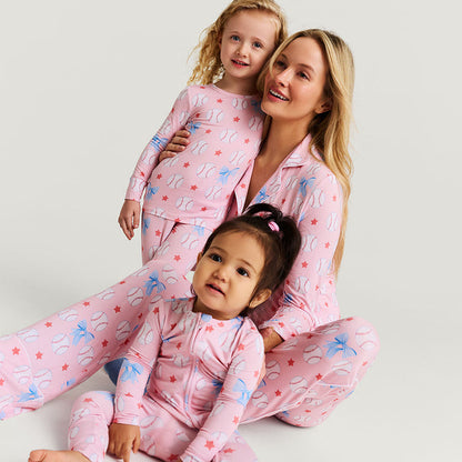 Woman and two children wearing matching pink pajamas with star and baseball patterns on a light gray background.
