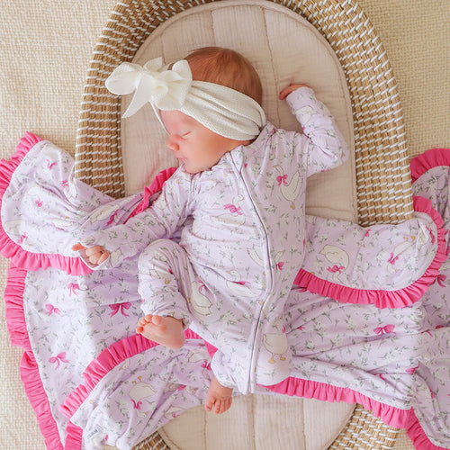Baby in a pink and light purple bamboo viscose one piece with a bow, lying in a wicker crib.