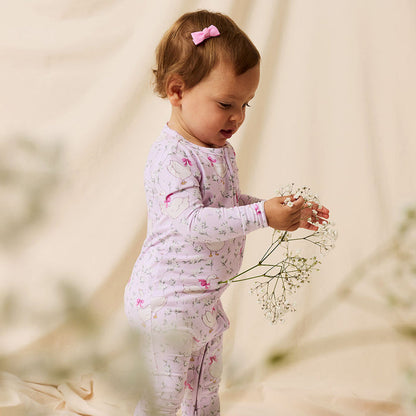 Child in a floral bamboo viscose one piece holding flowers against a blurred natural background
