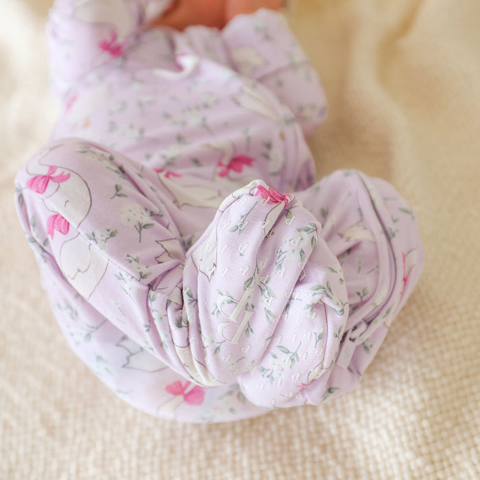 Baby feet in a pink floral one piece on a beige surface showing footsie detail with Posh Peanut logo.