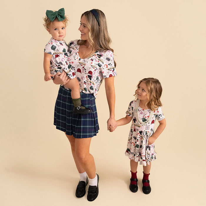 Woman holding a baby and standing next to a toddler, all wearing matching outfits on a beige background