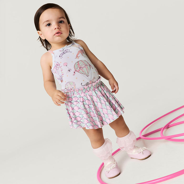 Child wearing a patterned dress with pink shoes on a light gray background