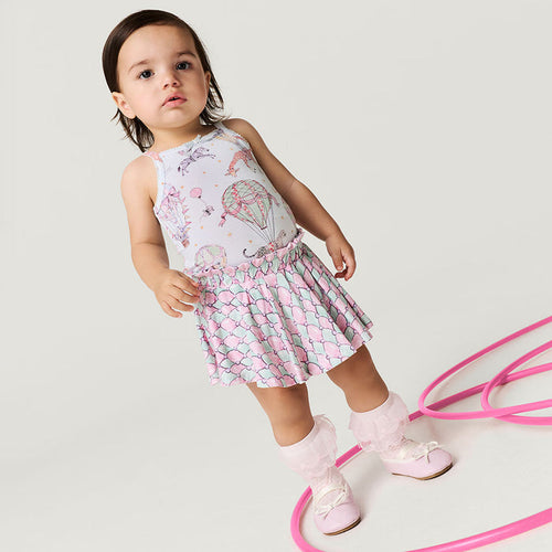 Child wearing a patterned dress with pink shoes on a light gray background