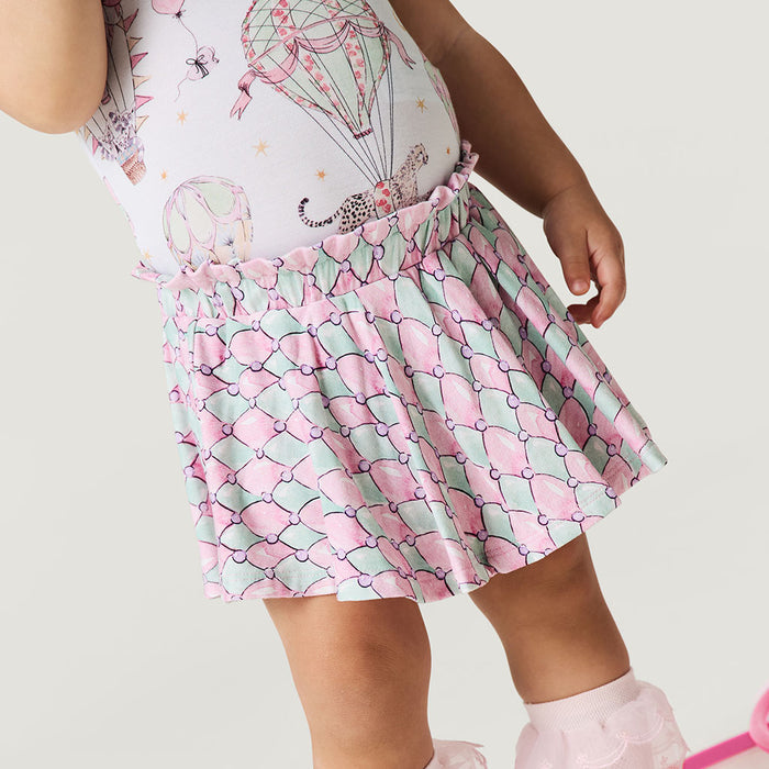 Child wearing a patterned dress with pink and green design on a plain background