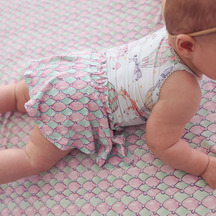 Baby in a patterned outfit lying on a pink and green checkered surface