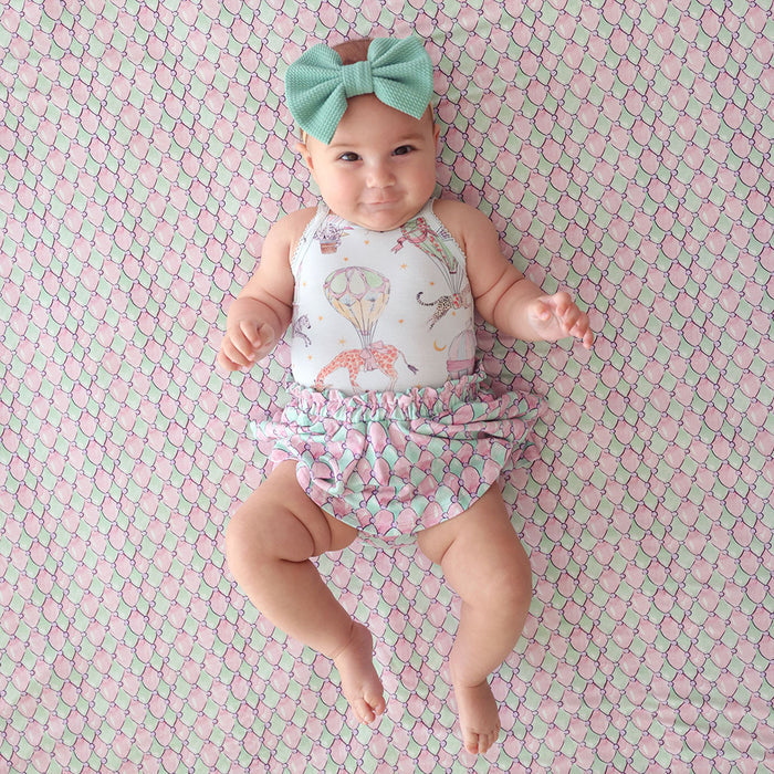 Baby wearing a patterned outfit and headband on a pink and green checkered background
