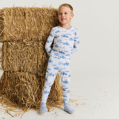Child wearing a blue and white patterned pajama set standing next to a stack of hay.