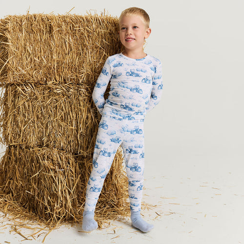 Child wearing a blue and white patterned pajama set standing next to a stack of hay.
