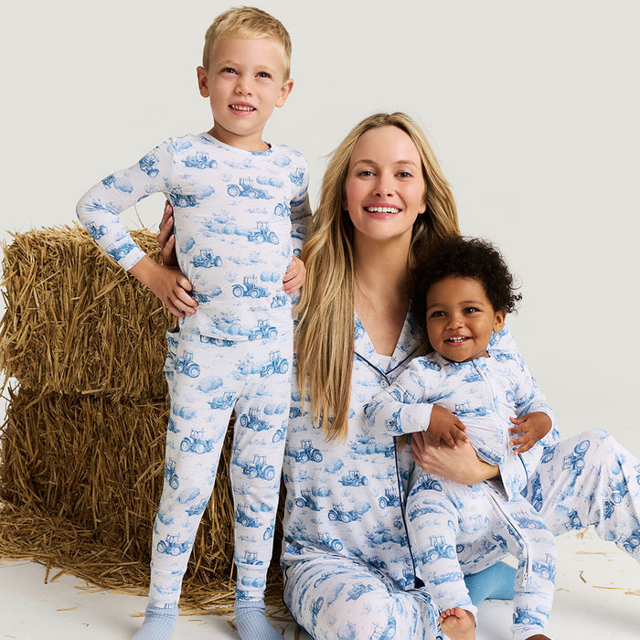 Woman and two children wearing matching pajamas with a blue tractor pattern on a white background.
