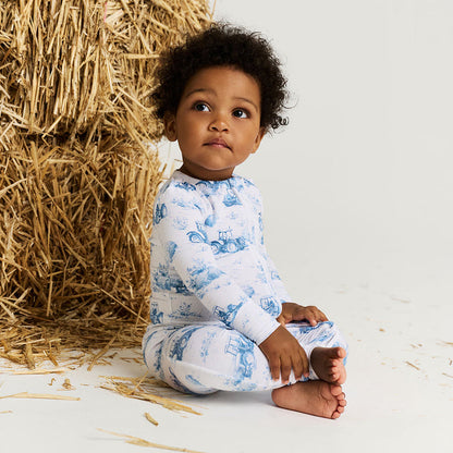 Child wearing blue and white pajamas sitting next to a bale of hay.