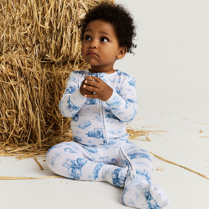 Child wearing a blue and white pajama set with train design, sitting next to a bale of hay.