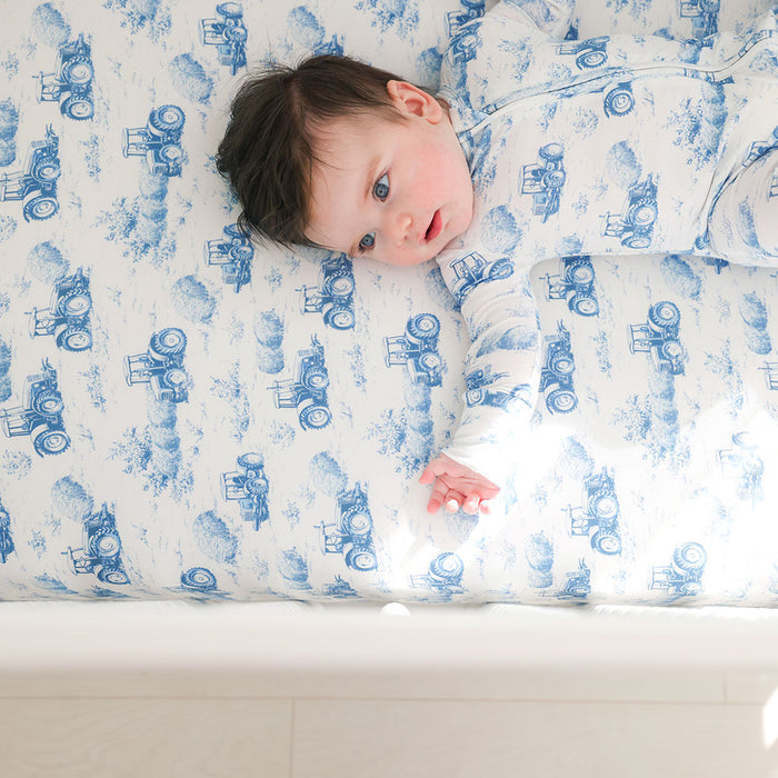 Baby lying on a mattress with blue tractor pattern