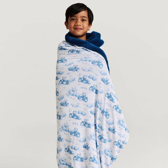 Child wrapped in a blue and white patterned blanket on a plain background