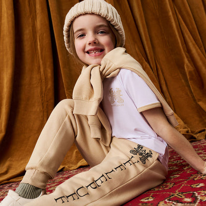 Child wearing tan Harry Potter Hufflepuff printed joggers with white tee and tan sweatshirt wrapped arounf shoulders.