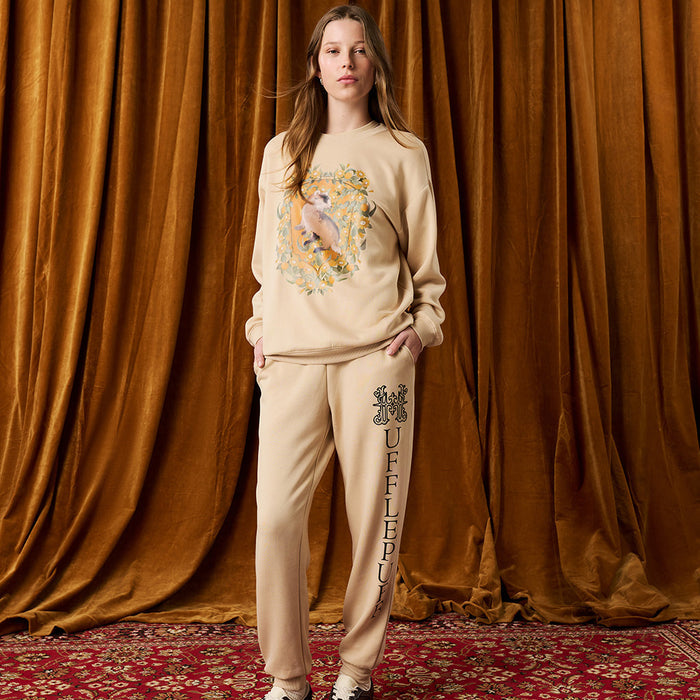 Person wearing a beige sweatshirt and pants with a design against a brown curtain background