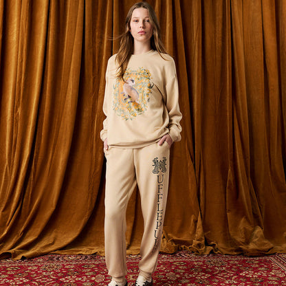 Person wearing a beige sweatshirt and pants with a design against a brown curtain background