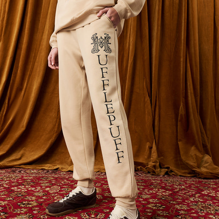 Person wearing beige 'Hufflepuff' sweatpants in front of a brown curtain.